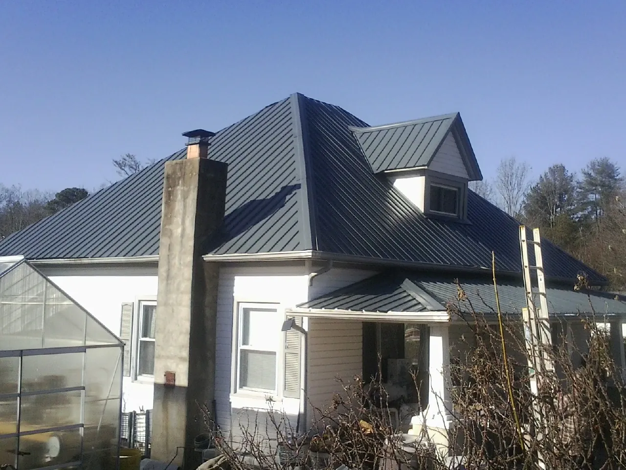 Dark blue standing seam metal roof on a white farmhouse with dormer — Slate & Tile Roof Repair by Roofing Brothers in Kemah
