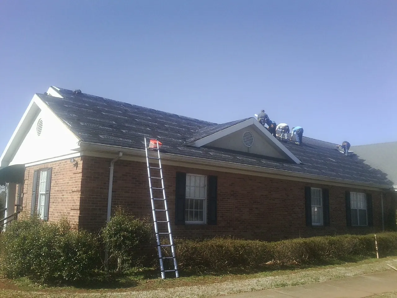 Crew tearing shingles off a brick ranch roof with a ladder set — Metal Roof Repair work by our crew in Kemah