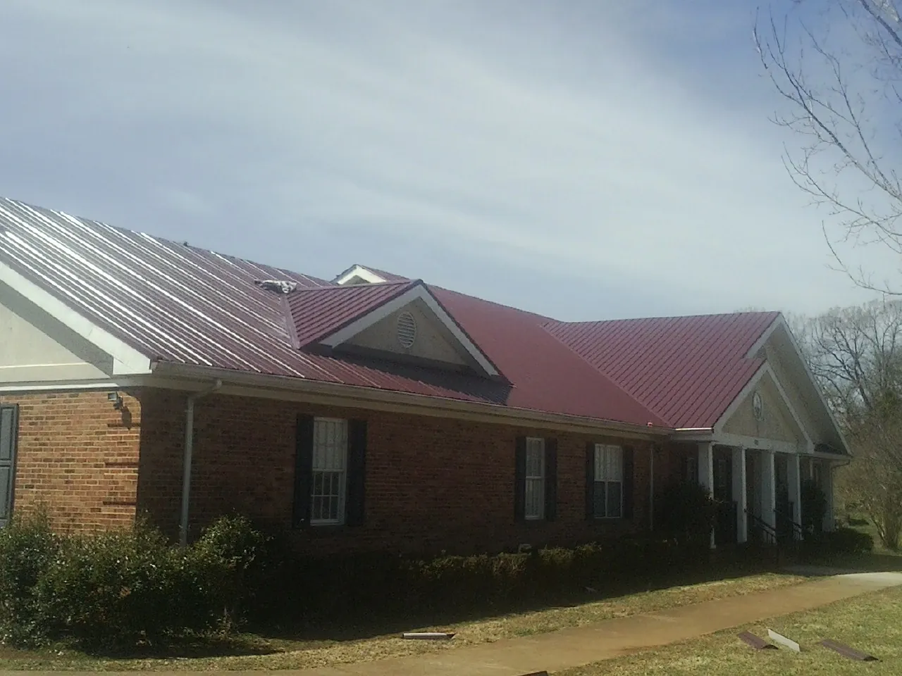 Red metal roof with gabled entries on a long brick building, from a Hail Damage Roof Repair job in Kemah