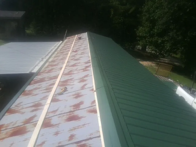 Old rusted panels beside newly installed green metal roofing — Wind Damage Roof Repair by Roofing Brothers in Kemah