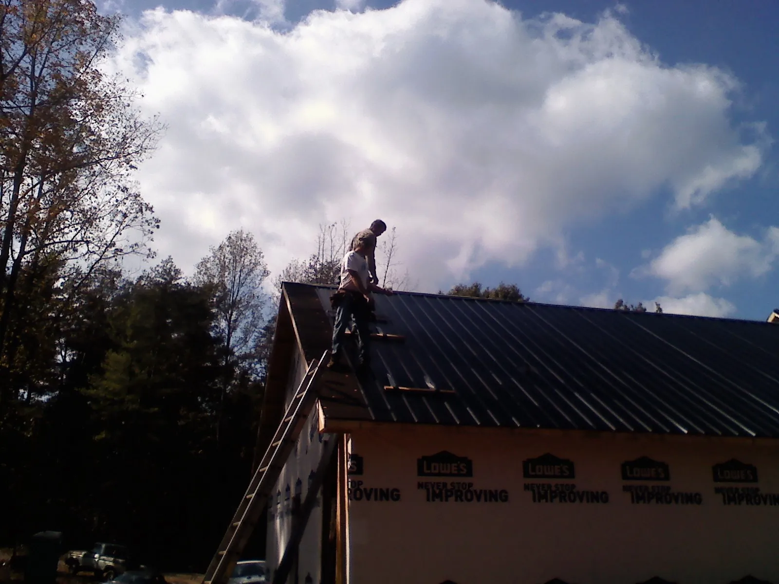 Roofer fastening dark metal panels high against a cloudy sky, from a Roof Inspection job in Kemah