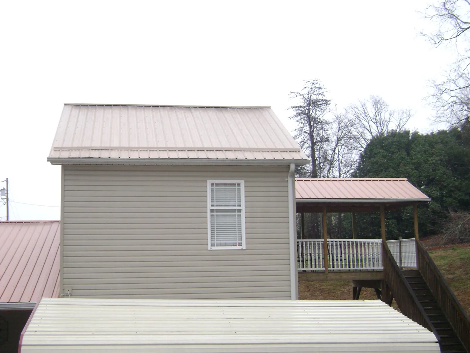 Tan metal roofs on a two story addition and attached porch, from a Roof Replacement job in Kemah
